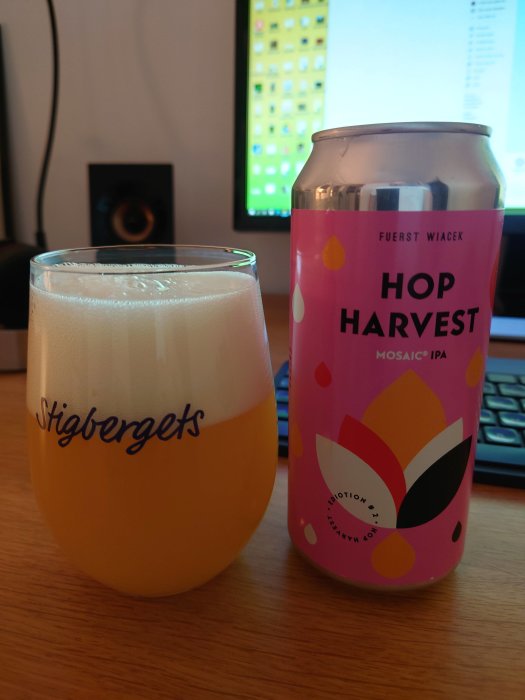 Ett ölglas märkt Stigbergets fyllt med öl och en burk Hop Harvest Mosaic IPA på ett skrivbord.