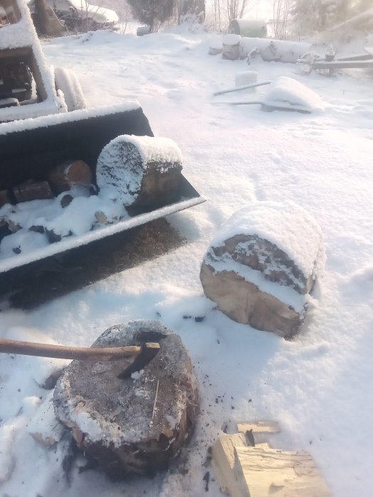 Snöig trädgård med nedkylt vedklabb av asp på marken och yxa för vedklyvning.