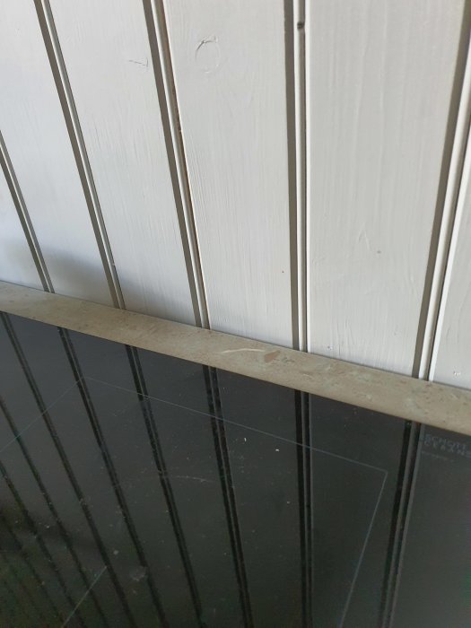 Kalkstensplatta redo att sättas som stänkskydd ovanför vit pärlspontvägg och svart spishäll.