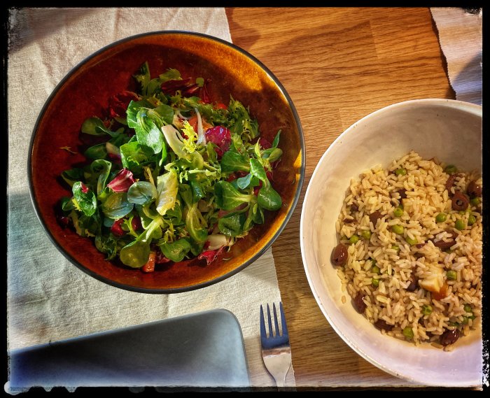 En skål med blandad provencesallad och en skål med risblandning med äppelbitar och oliver på ett träbord.