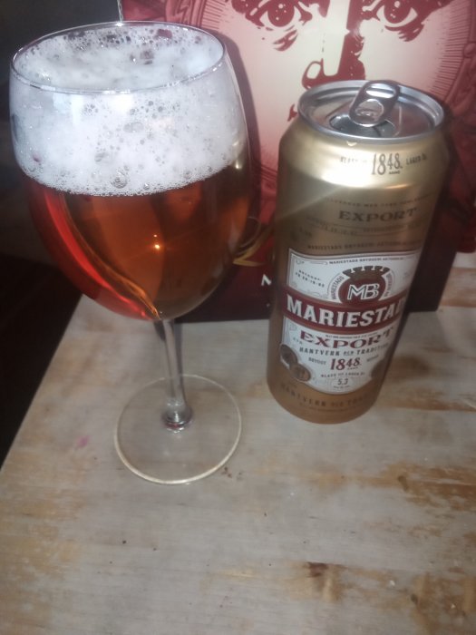 Ett glas fyllt med öl bredvid en burk Mariestad Export på ett träbord.