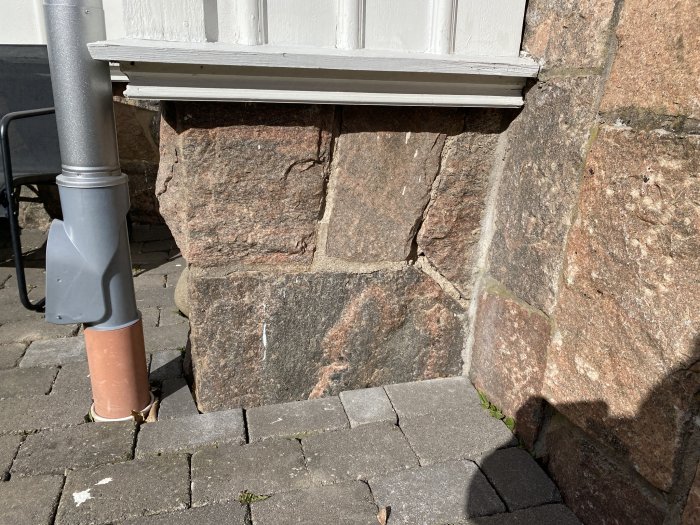Grundmur av granitblock med skadade fogar vid ett äldre hus, synlig stenstruktur och färgskillnader.