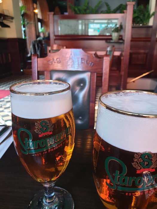 Två glas Staropramen öl på bord med inristad text 'The Big Ben' i bakgrunden.