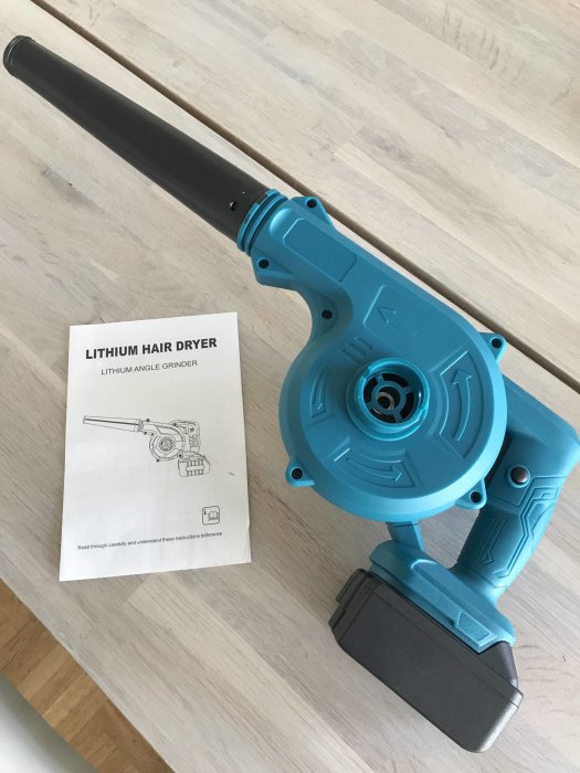 Blåsmaskin och instruktionsbok för en hår- och vinkelslipmaskin på ett träbord.