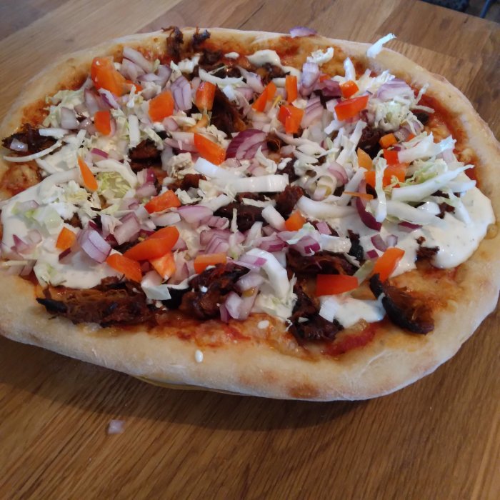 Kebabpizza med rödlök, isbergssallad och vit sås på en träskiva.