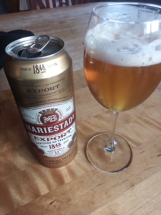 En burk Mariestads Exportöl bredvid ett glas öl på ett träbord, symbolisk för belöning efter städning.