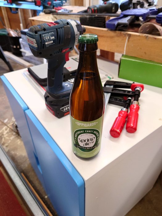 Flaska Öppigårds Spring Ale på arbetsbänk bredvid borr och skruvmejslar.