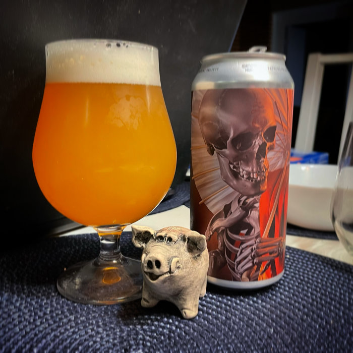 Ett glas med orange dryck bredvid en burk med skelettdesign och en liten grisfigur.
