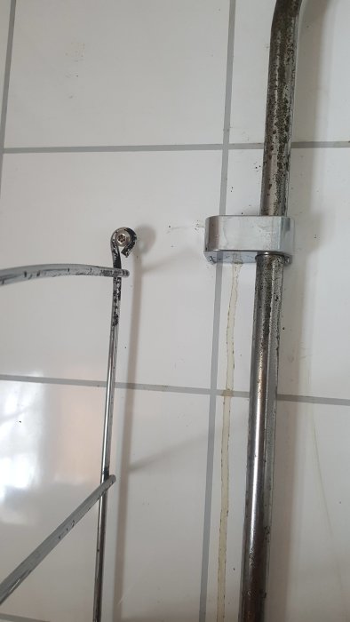Badrumsrör med svarta utfällningar, vit kakelvägg i bakgrunden.