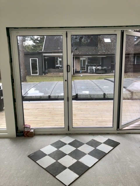 Kvadratiskt område med schackrutigt golv i diagonalt mönster framför en glasdörr som leder ut till en däckad terrass.