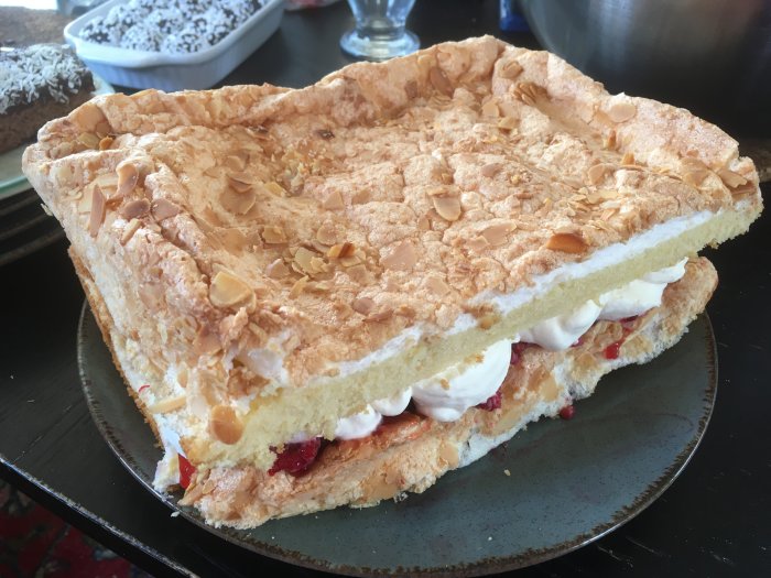 Pinocchiolayercake med jordgubbssylt, grädde och hallon, toppad med mandelflarn.