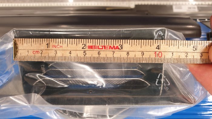 Linjal mäter lågprofilerad takhuv inslagna i plast, framför datortangentbord.