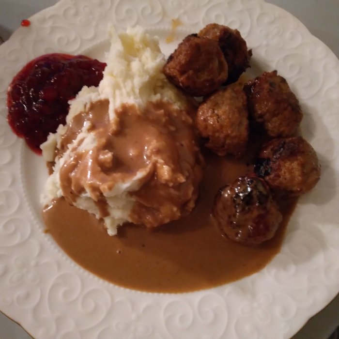 Ett måltid med köttbullar, potatismos, gräddsås och lingonsylt på en vit tallrik.