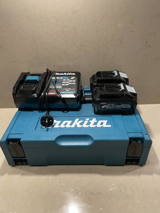 Makita-laddare och två 40V batterier på blå verktygslåda.