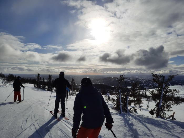 Skidåkare på ett snötäckt bergslandskap med solen som skiner genom molnen.