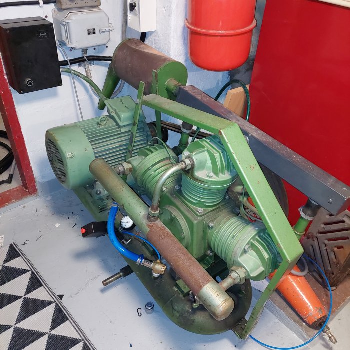 Begagnad grönmålad luftkompressor på 11 kW med separata tankar, installerad i en källare.