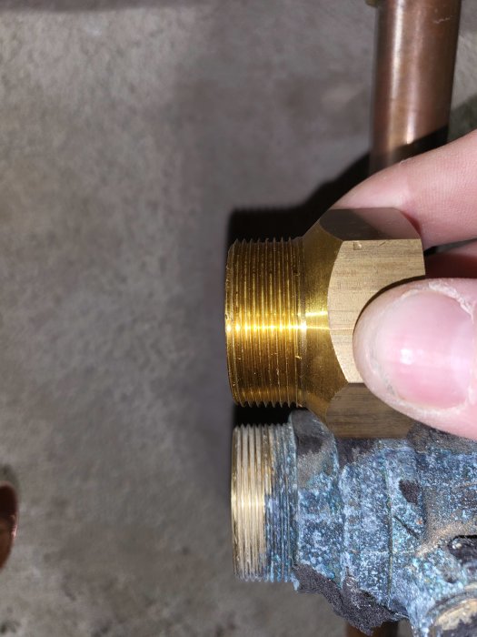 Hand som håller en klämring bredvid gängade rörkopplingar under installation av frikyla.