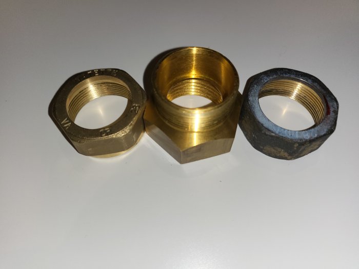 Tre mässingsfärgade kopplingsmuttrar av olika storlek, två ser nya ut och en är svartfärgad av användning.