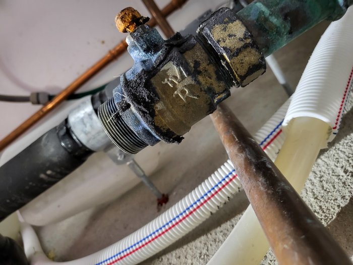 Gängad VVS-anslutning med saknad klämring och mutter, omgiven av rör i olika material och dimensioner.