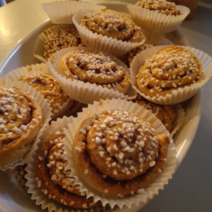 Hembakade kanelbullar med pärlsocker i formar på ett fat.