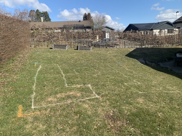 Trädgård med markerad yta för framtida växthus på lutande gräsmatta, omgiven av häck och staket.