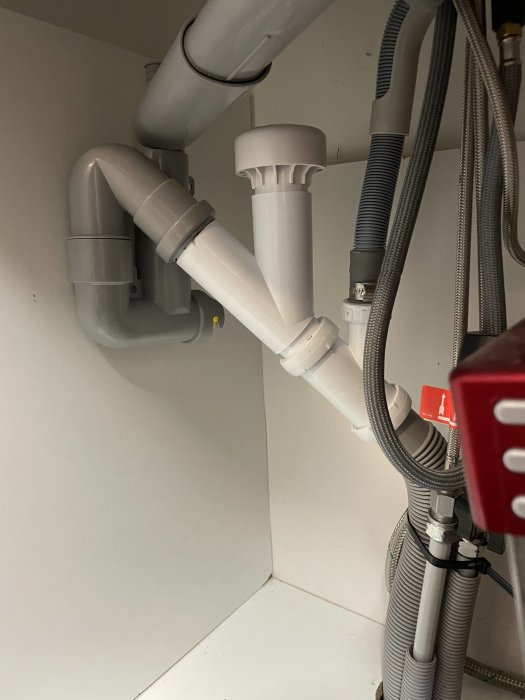 Installation av en ny vit vakuumluftare under en handfatsskåp, med anslutna rör och slangar för avloppssystemet.