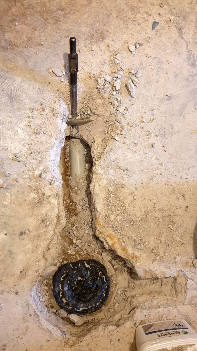 Spett fastkilat i betong bredvid avlopp och vattenrör under bilningsarbete i källare.