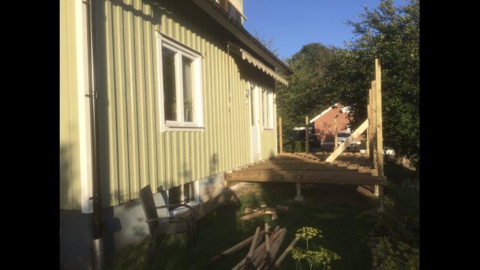 Bärlina fäst i hussockel under träpanel med nybyggd trätrappa och däck i solljus.