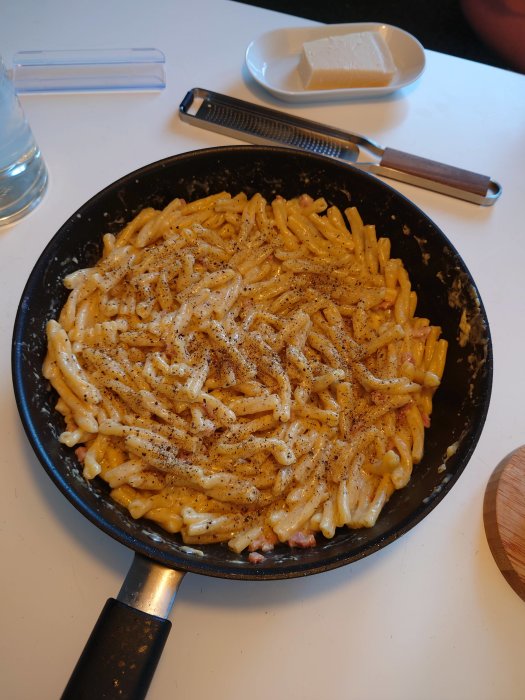 Krämig carbonara i stekpanna med rikligt med nymalen svartpeppar, serverad på köksbord.