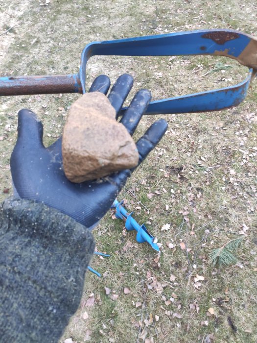 Hand i arbetshandske håller en sten med grusborr och vattenslang i bakgrunden.