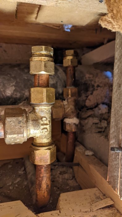 Rörmokeriarbete under golv med nyinstallerade kopparledningar och mässingsfittings.