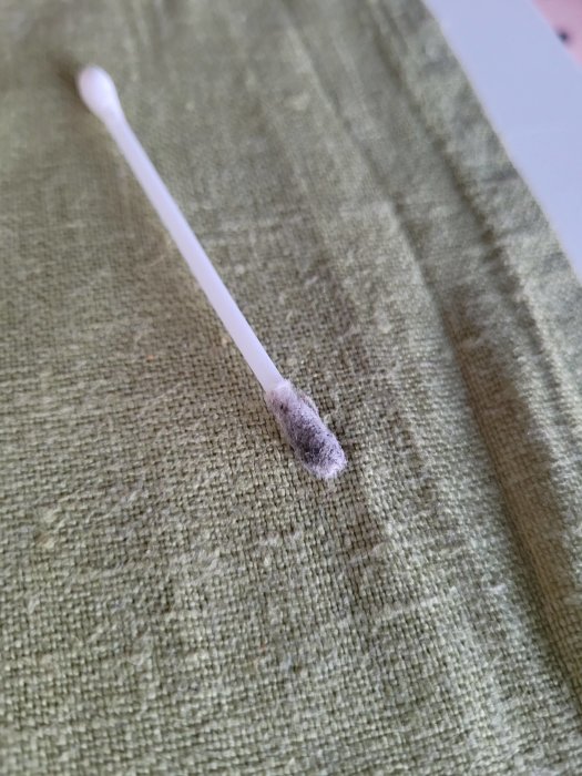 En bomullstopp med svart färg på en textil yta, efter test med T-röd för att identifiera akrylatfärg.