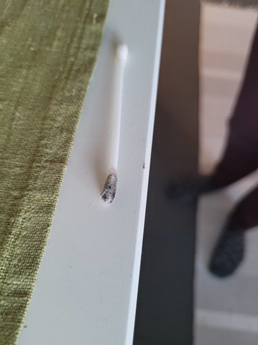 En tops med svarta fläckar ligger mot en vit kant av en möbel, indikerar test av akrylatfärg.