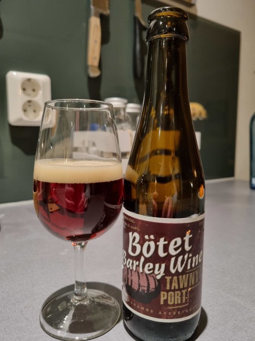 Flaska och glas med barley wine präglad av portvinsfatslagring på bord.