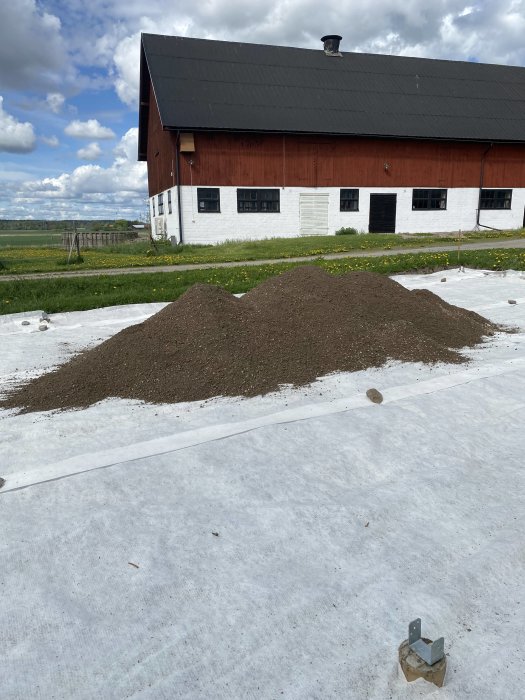 Två grushögar framför en röd ladugård med vita detaljer under en molnig himmel.