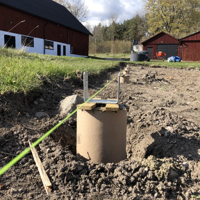 Papprör i mark med betong och stolpsko installerad, grön lina sträckt mellan stolpar under uppbyggnad.