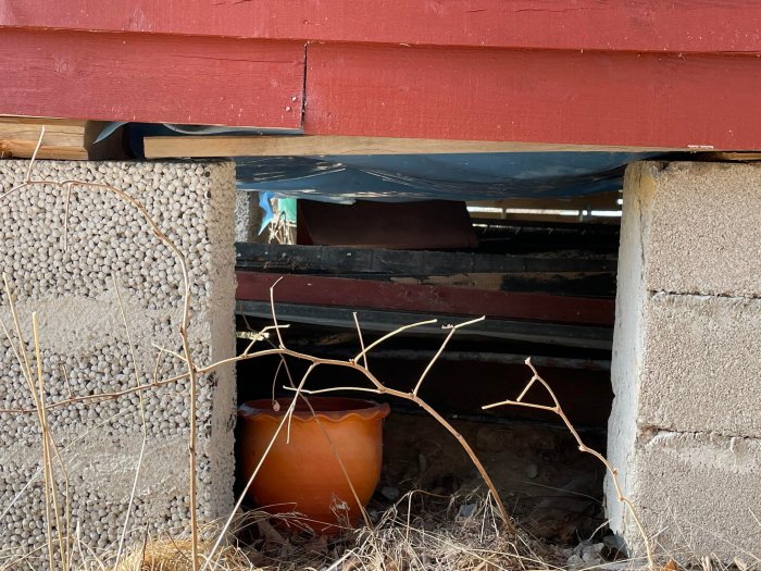 Bild på husgrund med lös plastmatta, snedställda pelare och luckrad jord som tyder på stabilitetsproblem.