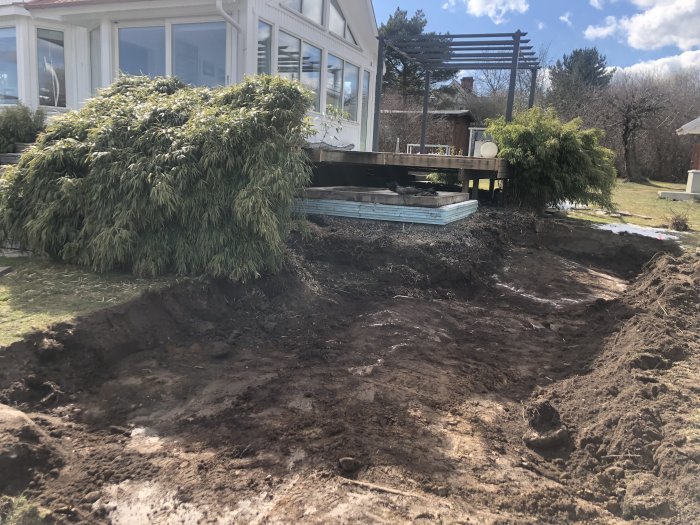 Uppgrävd trädgård med synligt berg och delvis byggd poolstruktur vid ett hus, redo för gjutning av pool.