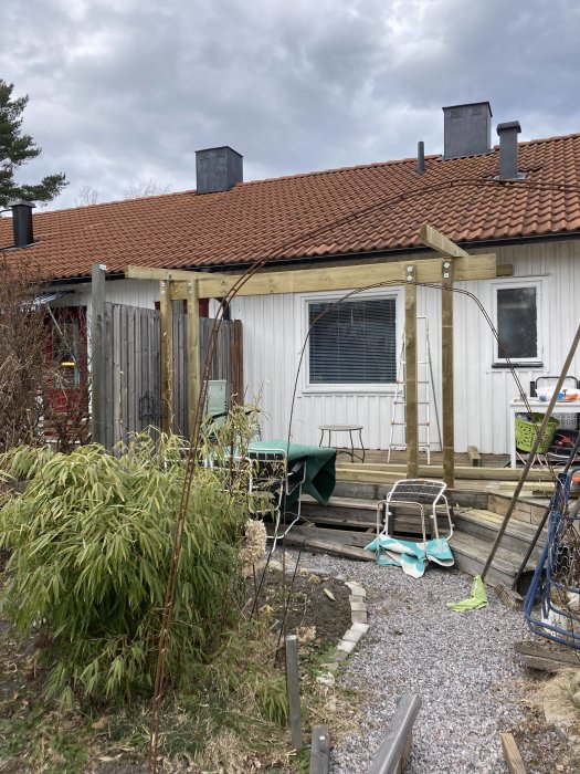 Altan under konstruktion med påbörjade stolpar och utplacerat byggmaterial framför hus.