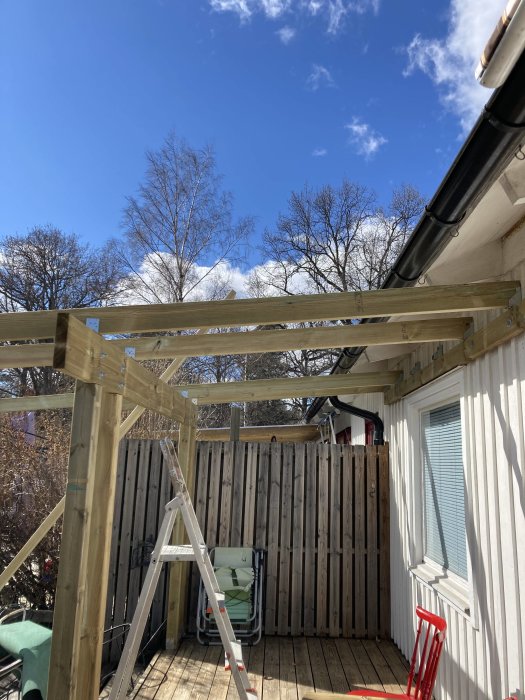 Påbörjat bygge av uterum med trästolpar och bärlina på befintlig altan, stege synlig.