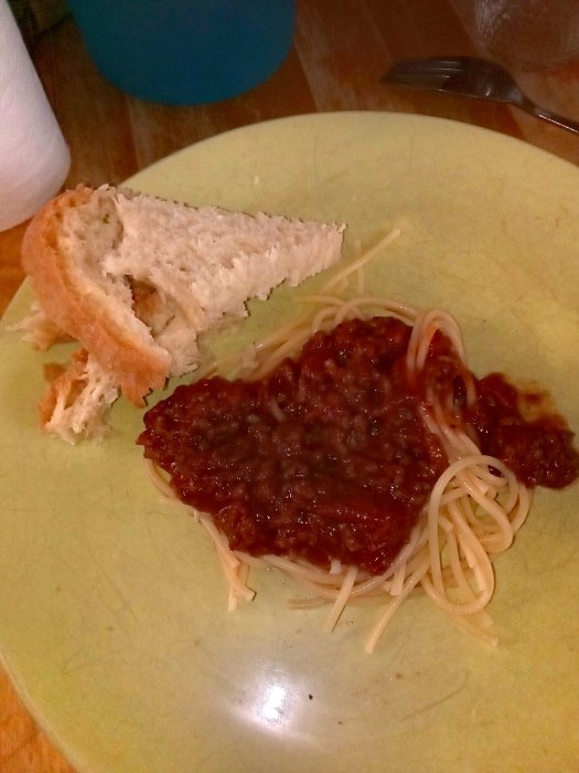 Hemlagad spaghetti med köttfärssås och ett stycke bröd på en grön tallrik.