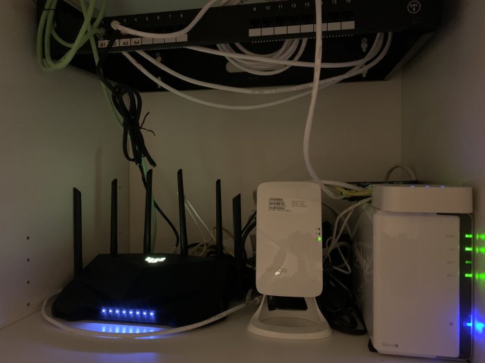 ASUS TUF-AX5400 router med flera antenn och blinkande lampor i ett IT-skåp bredvid annan nätverksutrustning.