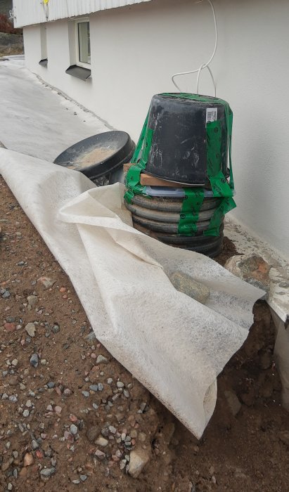 En provisorisk installation av en kanalfläkt i en dräneringsbrunn utanför en byggnad för att minska radonvärden.
