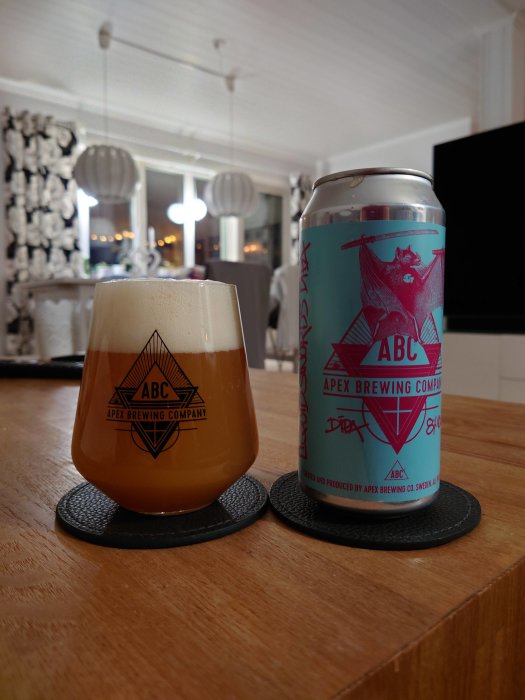 Ölglas märkt "Apex Brewing Company" och en burk Apex DIPA på ett bord i ett hem.