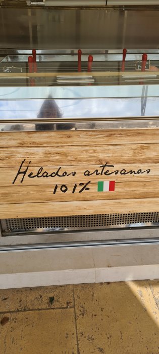 Glasskylt med texten "Helado artesano 101%" och Italiens flagga på en glassdisk.