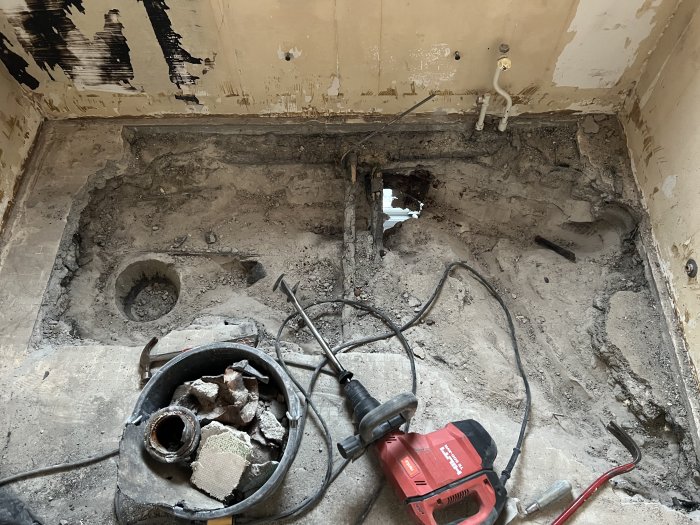 Renoveringsarbete i badrum med uppbrytet golv och väggar samt rivningsavfall och verktyg.