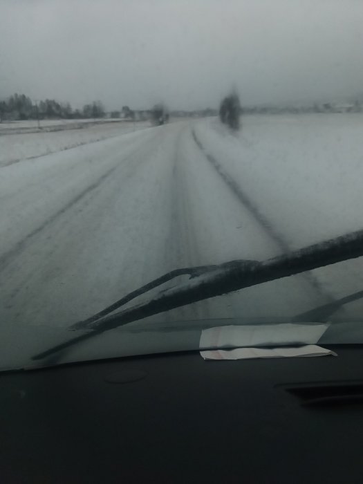 Vy från bilens insida av en snöig och isig väg med synliga däckspår.