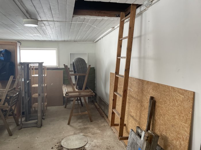 Gammalt rum som förbereds för renovering med synliga takbjälkar, staplade stolar och byggmaterial.