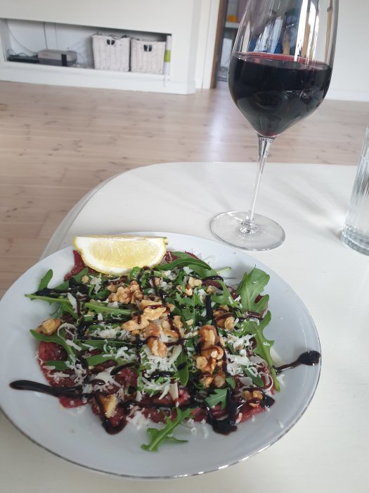 En tallrik med rödbetssallad med ruccola, valnötter och riven ost, serverad med ett glas rött vin.