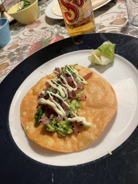 Friterad majstortilla toppad med guacamole, hackad tonfisk, sesamfrö, lime och chipotlemajonnäs på en tallrik.